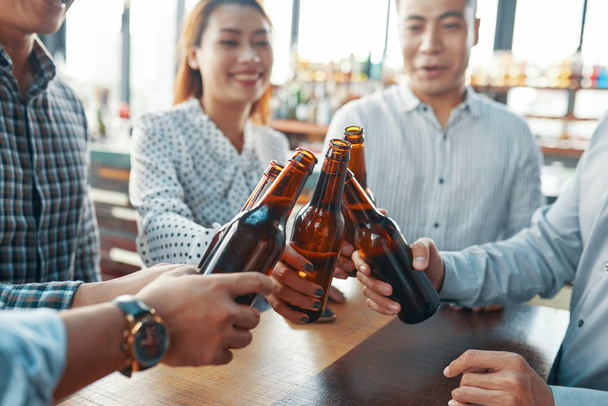 Erntehelfer versammeln sich und stoßen mit Bierflaschen auf Erfolg in Bar an - Foto, Bild