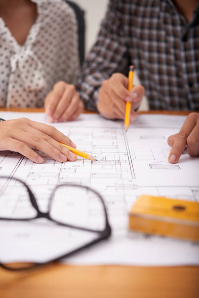 Ręce nierozpoznawalnych współpracowników z ołówków wskazujących na planie budynku podczas pracy w biurze razem - Zdjęcie, obraz