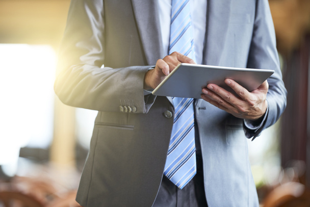 Close-up de executivo do sexo masculino de terno em pé e segurando tablet digital, ele digitando uma mensagem ou trabalhando online
  - Foto, Imagem
