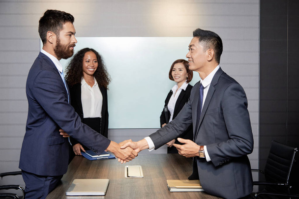 Uśmiechnięci partnerzy biznesowi potrząsając rękami przed rozpoczęciem spotkania - Zdjęcie, obraz