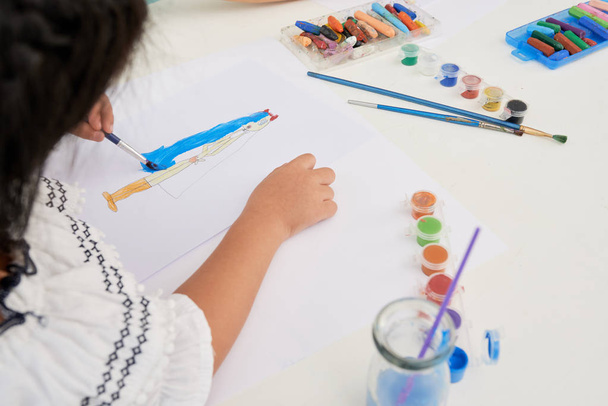 Nerozpoznatelná holčička, která sedí u stolu a kresí s akvarel v umělecké třídě - Fotografie, Obrázek