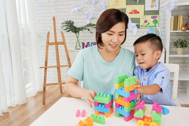 Усміхнений вчитель азіатських жінок і хлопчик грає з барвистими будівництво набір в арт-класі - Фото, зображення