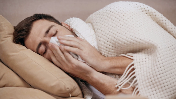 όμορφος άρρωστος άνθρωπος ξαπλωμένος στο κρεβάτι, βήχας, παίρνοντας ιστό και φυσώντας τη μύτη στο σπίτι - Πλάνα, βίντεο