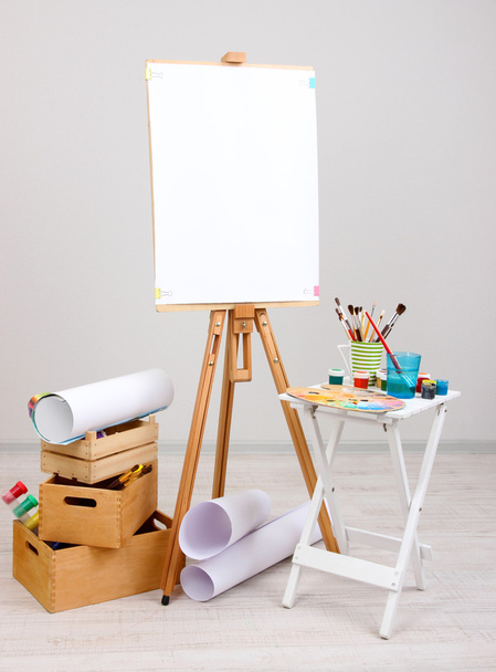 Wooden easel with clean paper and art supplies in room - Fotografie, Obrázek