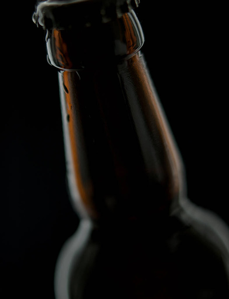 schwarze Bierflasche mit Wassertropfen isoliert auf schwarzem Hintergrund mit Leerzeichen - Foto, Bild