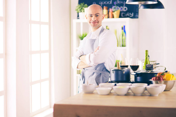 Yakışıklı adam mutfakta yemek yapıyor ve gülümsüyor. - Fotoğraf, Görsel