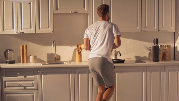 pohledný vousatý muž s úsměvem a tancem v moderní kuchyni  - Záběry, video