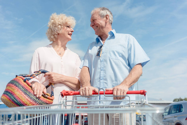 Senior man met een winkelwagentje tijdens het kijken naar zijn vrouw met liefde - Foto, afbeelding
