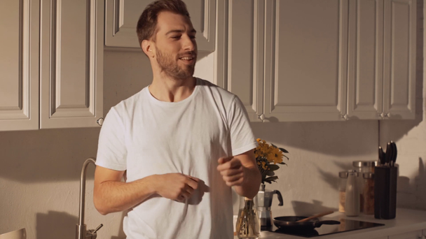 όμορφος μουσάτος άνθρωπος χαμογελαστός, παλαμάκια και χορεύοντας στη σύγχρονη κουζίνα  - Πλάνα, βίντεο