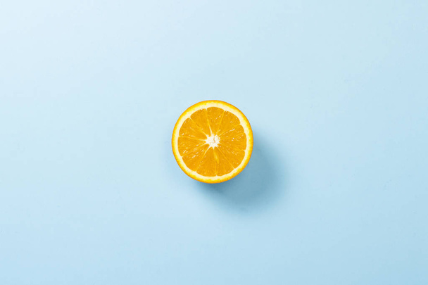 Cut half of orange on a blue background. Minimalism. Concept of tropics, healthy eating, vitamins. Flat lay, top view. - Foto, Imagen