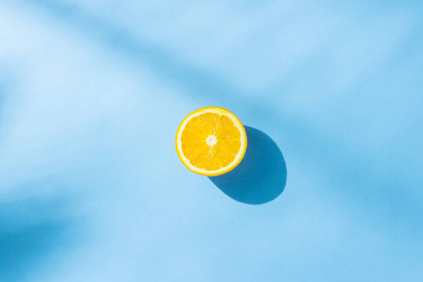 Orange on a blue background under natural light with shadows. Hard light. Concept of diet, healthy eating, rest in the tropics, vacation and travel, vitamins. Flat lay, top view. - Photo, Image