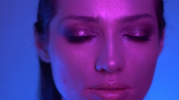 Extraordinary fashion model in colorful purple and blue neon lights posing into camera in studio watching rightwards. - Felvétel, videó