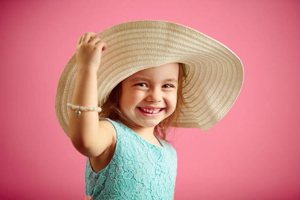 Isolated portrait of little girl in panama hat, smile, holds hand hat, stands on pink isolated background. - Foto, afbeelding