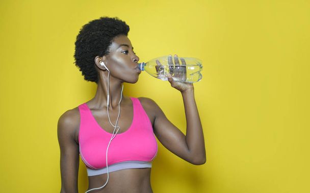 beautiful african american woman in sports bra and headphones drinking water - Foto, Imagen