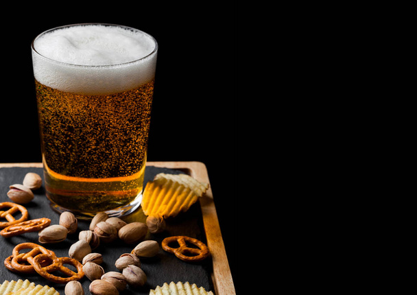 Bicchiere di birra lager con spuntino su tavola di pietra su sfondo nero. Pistacchi e pretzel con patatine fritte. Spazio per testo
 - Foto, immagini