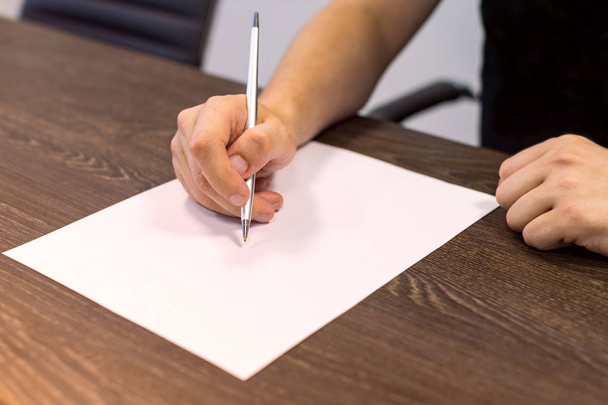 Empresario sentado en la mesa y sostiene la pluma en la mano derecha. Hay una hoja de papel en blanco sobre la mesa. Concepto foto
. - Foto, imagen