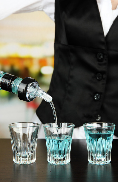 Barmen hand with bottle pouring beverage into glasses, on bright background - Photo, image