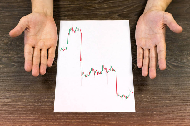 Man sitting at table. There are sheet of paper with a trading chart on the table. Misunderstanding gesture with hands. Concept photo. - Photo, image