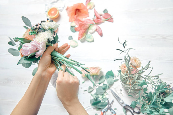 Top view cropped image of female florist arranging a bouquet with flowers use tools on white woodem background. Flowers delivery. Copy space. workplace and professional concept - Фото, изображение