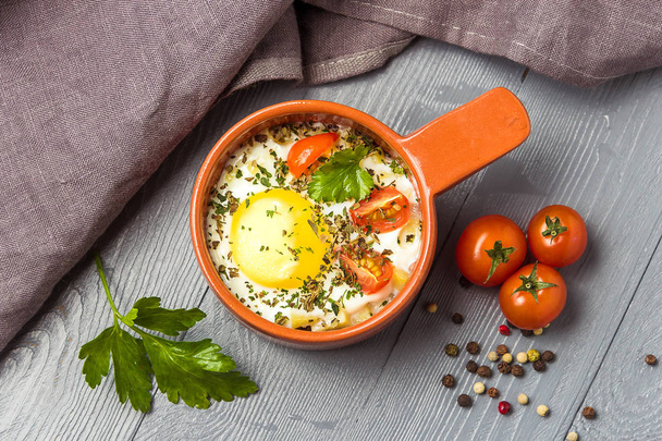 Portioned baked eggs in ceramic cocotte on gray wooden table, breakfast. Top view. - Foto, Imagem