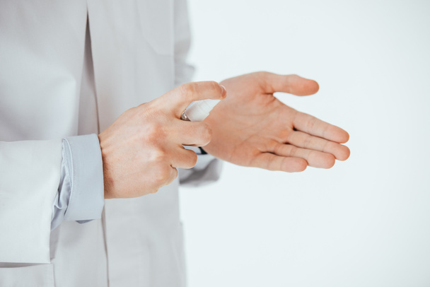 oříznutý pohled lékaře aplikoval antibakteriální sprej na ruku izolovaný na bílém  - Fotografie, Obrázek