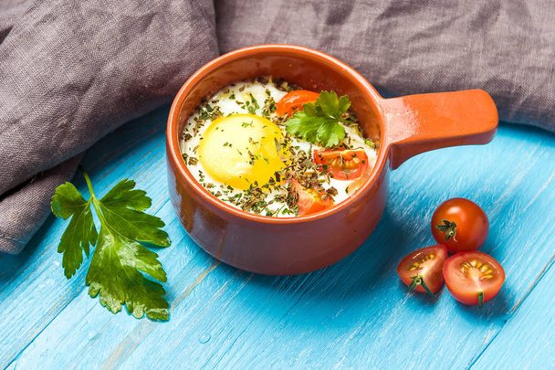 Portioned baked eggs in ceramic cocotte on blue wooden table, breakfast. - Foto, Imagen