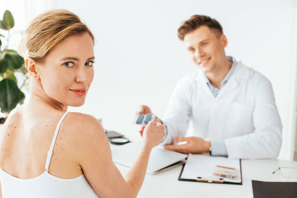 selective focus of attractive woman holding pills near cheerful doctor  - Fotó, kép