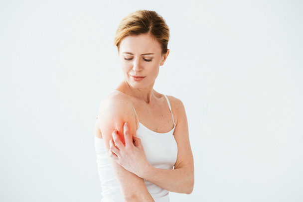 όμορφη αλλεργική γυναίκα ξύσιμο κόκκινο δέρμα στο χέρι, ενώ στέκεται στο λευκό  - Φωτογραφία, εικόνα