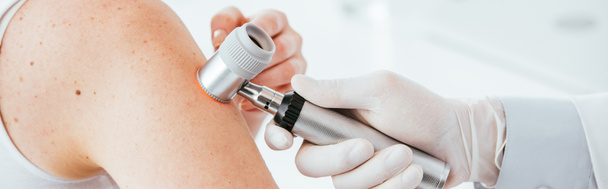 panoramic shot of dermatologist in latex glove holding dermatoscope while examining patient  - Fotografie, Obrázek
