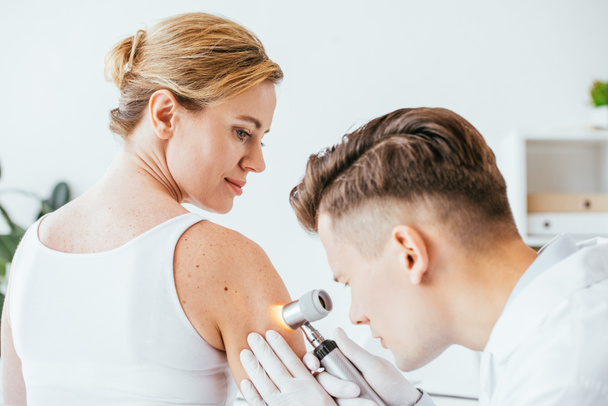 dermatologist in latex gloves holding dermatoscope while examining beautiful woman with skin disease   - Fotografie, Obrázek