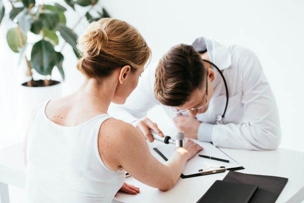 επιλεκτική εστίαση της γυναίκας που κοιτάζει τον δερματολόγο που εξετάζει το δέρμα στην κλινική  - Φωτογραφία, εικόνα