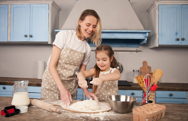 ευτυχισμένη οικογένεια ετοιμάζει το αρτοποιείο μαζί. Η μητέρα και το παιδί κόρη κορίτσι φτιάχνουν μπισκότα και διασκεδάζουν στην κουζίνα. Η μητέρα διδάσκει την κόρη της να ζυμώνουν τη ζύμη στο τραπέζι της κουζίνας - Φωτογραφία, εικόνα