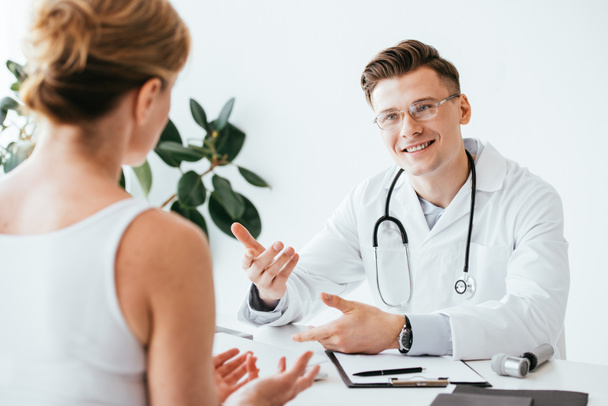 selective focus of cheerful doctor in glasses and white coat gesturing while looking patient  - Foto, Bild