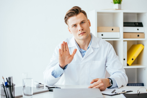 handsome and serious doctor in white coat gesturing in clinic  - Photo, image