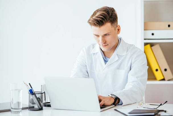 красивий лікар у білому пальто під час використання ноутбука в клініці
  - Фото, зображення