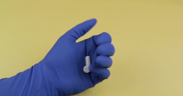 Witte pillen in de hand gekleed in blauwe medische handschoen. Vrouw neemt een ronde pil - Video