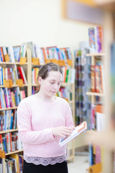  girl of 13 years old choosing   book in   library.  - Fotó, kép