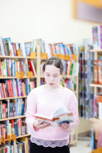 Roztomilá dívka ve veřejné knihovně u policích s knihami. - Fotografie, Obrázek