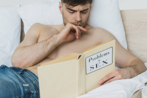 messa a fuoco selettiva di pensoso uomo a torso nudo che legge problemi nel libro di sesso mentre si trova a letto
 - Foto, immagini