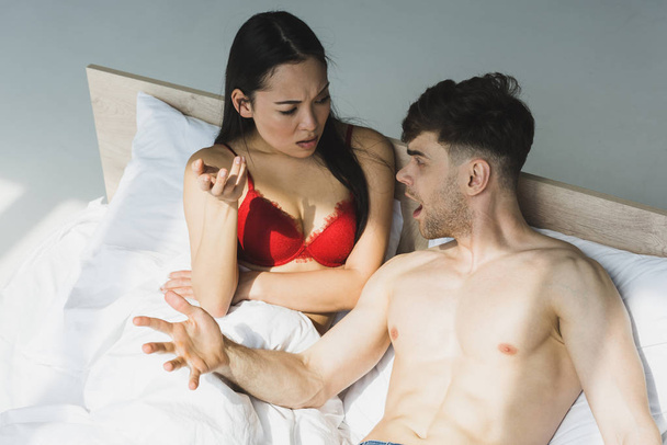 pohledný muž bez košile, hádaný s krásnou asijskou přítelkyní v červeném prádle - Fotografie, Obrázek