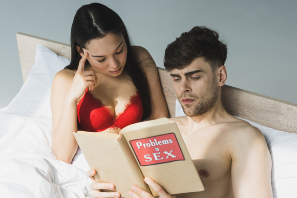 keskittynyt monikulttuurinen pari lukeminen ongelmia seksikirja kun makaa sängyssä auringonvalossa
 - Valokuva, kuva