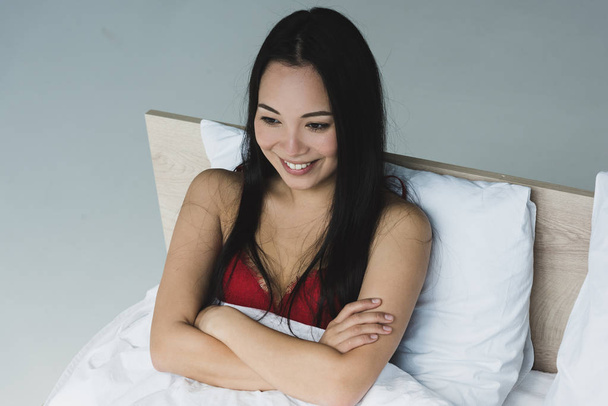 kırmızı sütyen güzel asyalı kadın çapraz kolları ile yatakta yatarken gülümseyen - Fotoğraf, Görsel