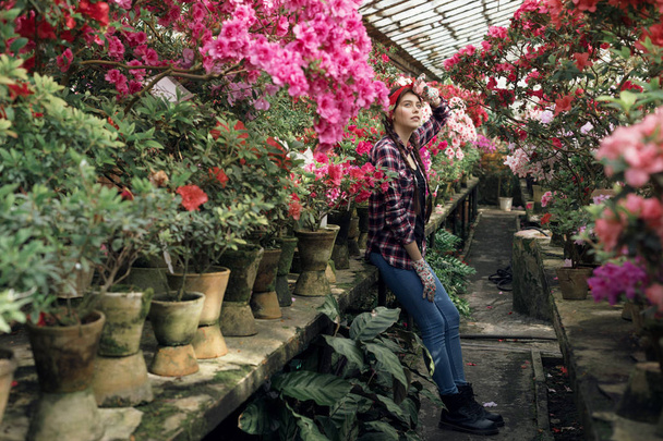 Krásná mladá žena zahradnice s copánky a červeným hlavním pásem, která odpočívá po tvrdé práci s jarní květinou ve skleníku - Fotografie, Obrázek