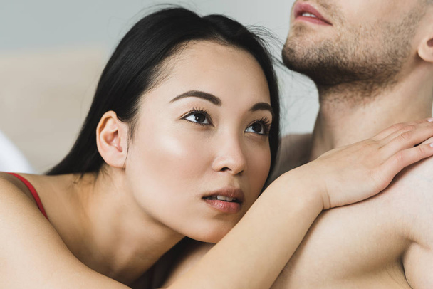 gedeeltelijke weergave van de mens met mooie peinzende Aziatische vriendin liggend op zijn borsten - Foto, afbeelding