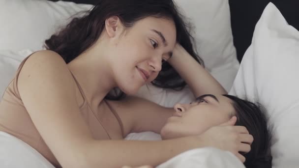 Lesbische paar knuffelen en glimlachend terwijl ze samen liggen in bed thuis. Jonge lesbiennes kussen en knuffels na wakker - Video