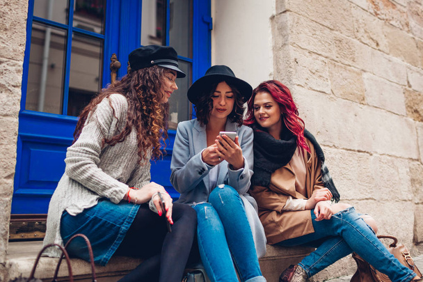 路上でスマートフォンを見ている3人の若い女性の屋外ショット。女の子が話し、楽しんで - 写真・画像