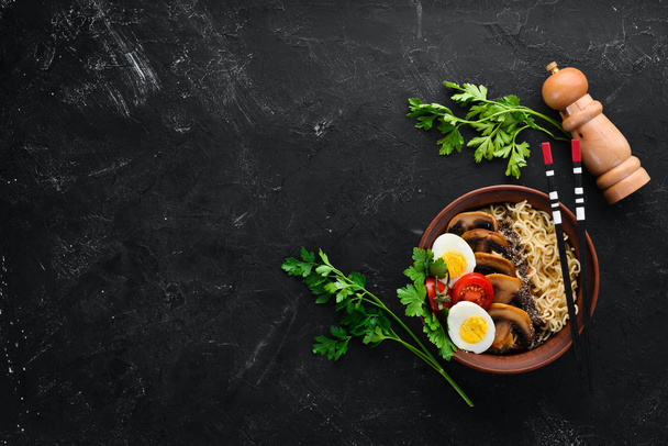 Asian food. Noodles with mushrooms, eggs and chia seeds. On a black stone background. Top view. Free copy space. - 写真・画像