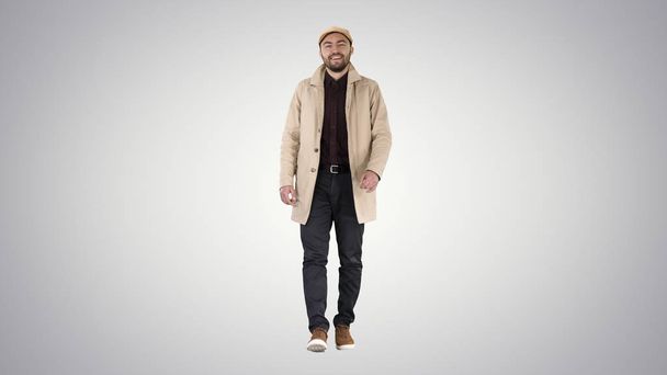 Handsome man in fashionable clothes walking and smiling on gradient background. - Фото, изображение