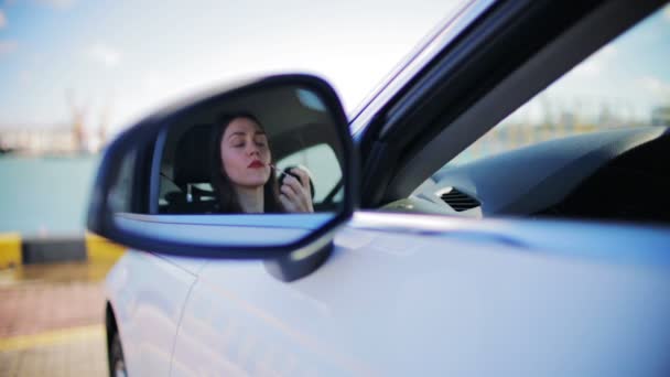 mladá krásná žena klade červenou rtěnku na rty odraz v autě boční zrcadlo proti hlubokému modrému moři - Záběry, video