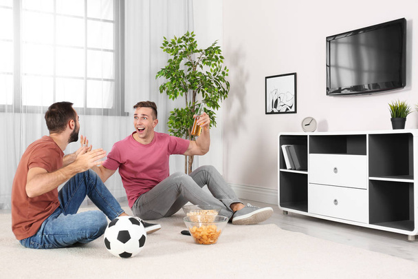 Young men watching TV while sitting on floor at home. Sport channel - Foto, Imagen